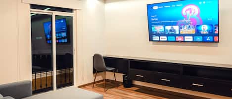 Una sala de estar moderna con un televisor de pantalla plana montado en la pared, un sofá gris, una mesa de centro de madera y un cubo de basura negro.