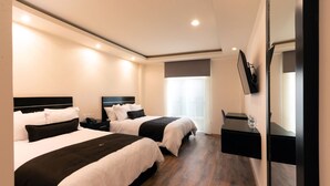 Quarto de hotel com duas camas, uma mesa de cabeceira com telefone, uma mesinha com um copo de água e uma TV na parede.
