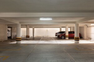 Un aparcamiento con pilares de hormigón, un coche rojo estacionado y una luz fluorescente en el techo.
