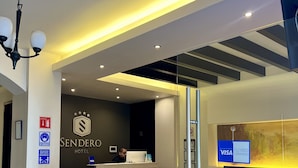 Uma área de recepção de hotel com design moderno, incluindo um balcão de atendimento, uma área de estar com um sofá e cadeiras, e um painel de vidro.