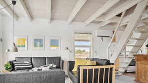 A modern living room with a grey sofa, a wooden chair, and a staircase leading to an upper level. - "Andrine" - 700m from the sea by Interhome (Henne)