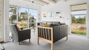 A modern living room with a sofa, armchair, and large windows offering a view of the outdoors. - "Andrine" - 700m from the sea by Interhome (Henne)