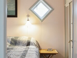Un dormitorio con cama, mesita de noche, lámpara, ventana y puerta.