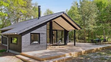 Une cabane moderne dotée d’un toit en pente, de grandes fenêtres et d’une terrasse.