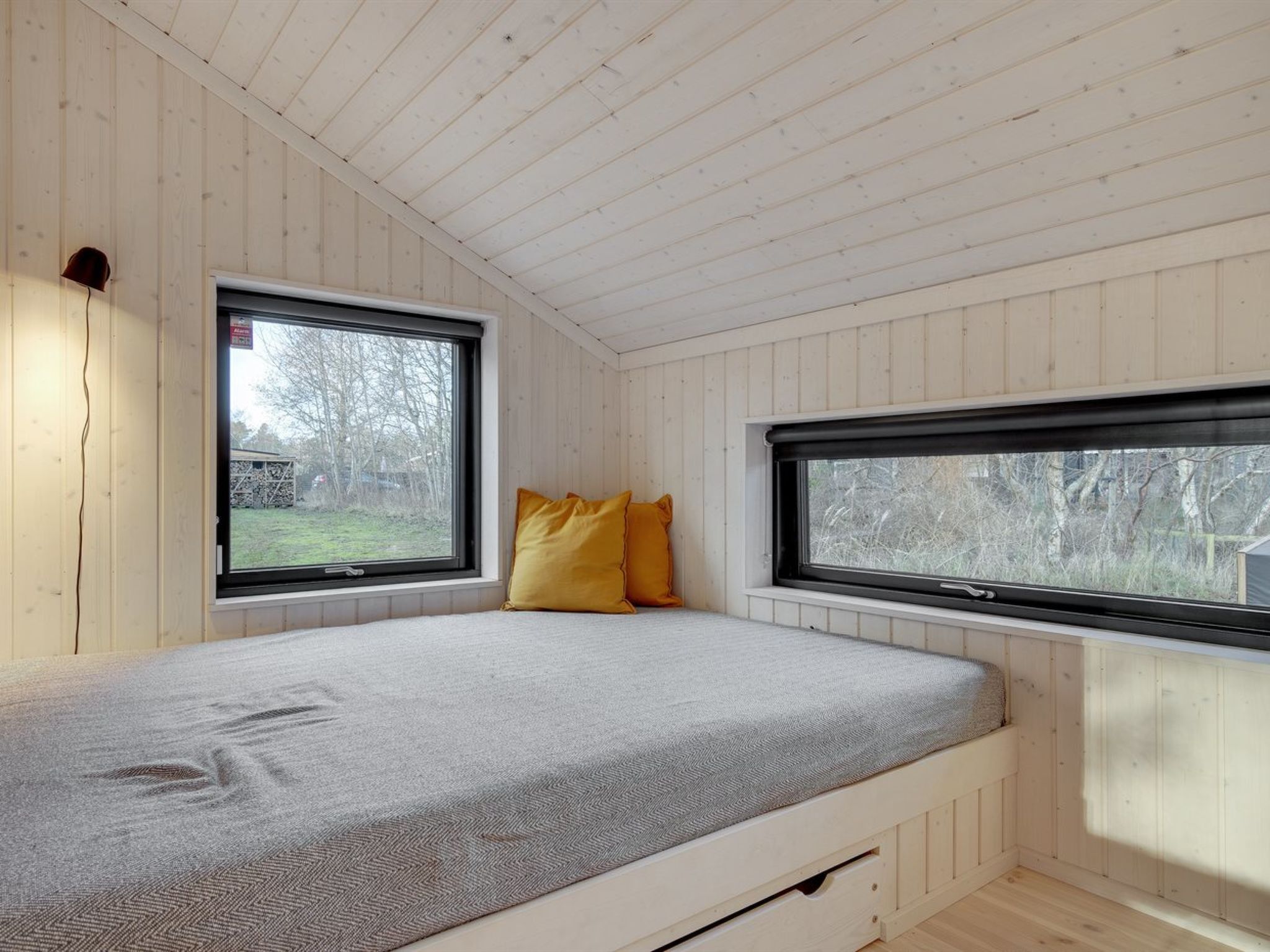 A bedroom with a bed, two windows, and wooden walls.