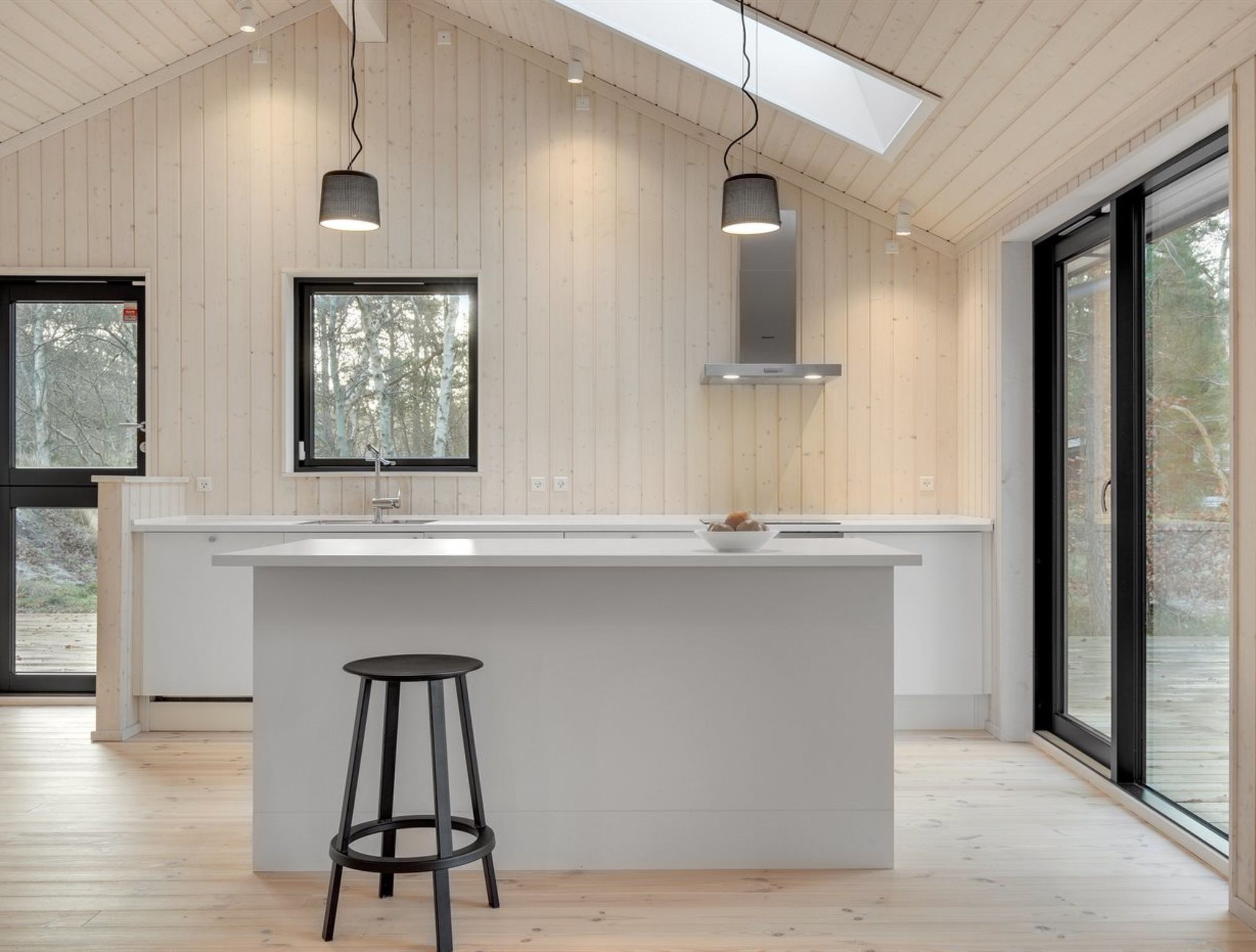 Une cuisine moderne dotée d’un îlot central, de luminaires suspendus et de grandes fenêtres.