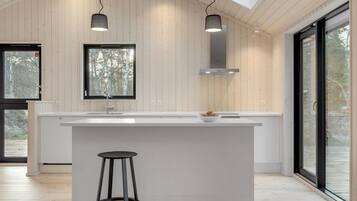 Une cuisine moderne dotée d’un îlot central, de luminaires suspendus et de grandes fenêtres.