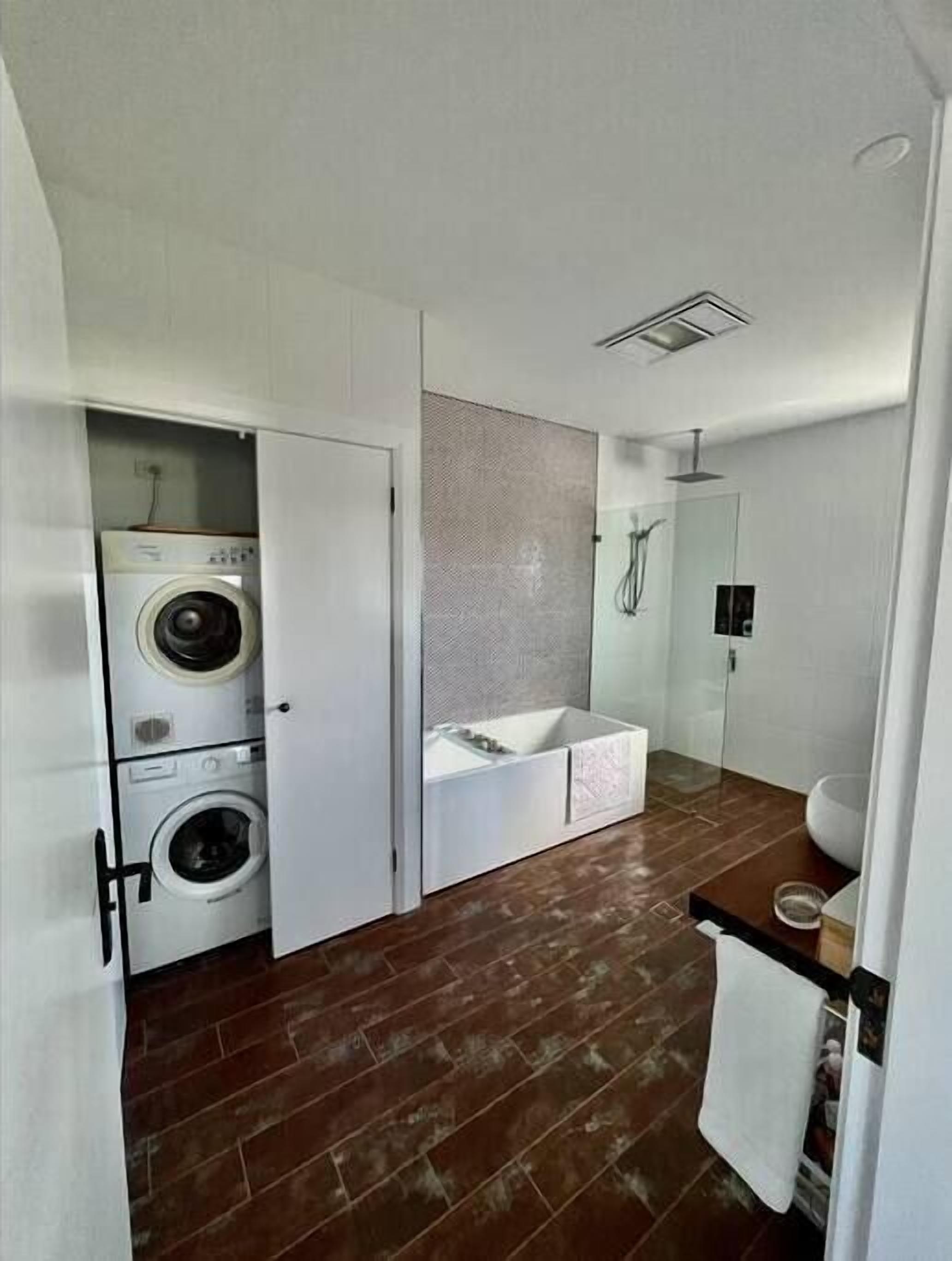 A compact, modern bathroom with a built-in washer and dryer, a large mirror, and a shower area.