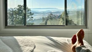 Une chambre à coucher dotée d’une grande fenêtre donnant sur un paysage vallonné.