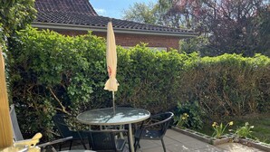 Een terras buiten met twee ronde tafels en stoelen, een witte parasol en een stenen huis op de achtergrond.