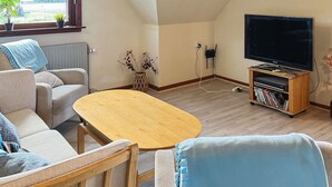 Een knus woongedeelte met een bank, een salontafel, een tv-meubel met een flatscreen televisie en een boekenkast.