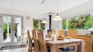 A modern dining area with a wooden table and chairs, a built-in stove, and large windows offering a view of the outdoors.