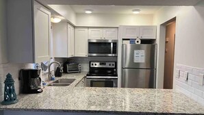 A compact kitchen with white cabinets, a microwave, a toaster, a coffee maker, and a refrigerator. - Perfect 2/1 beach duplex apartment in the heart of STA beach (St. Augustine)