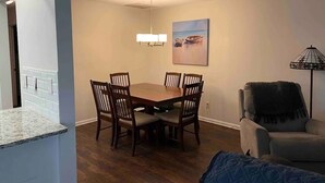 A dining area with a wooden table and chairs, a chandelier, a painting on the wall, and a lamp. - Perfect 2/1 beach duplex apartment in the heart of STA beach (St. Augustine)