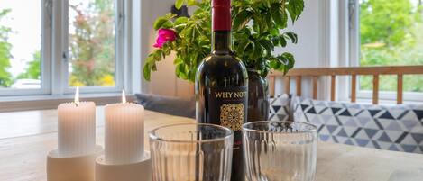 A table with candles, a bottle of wine, and glasses, with a window and a plant in the background.