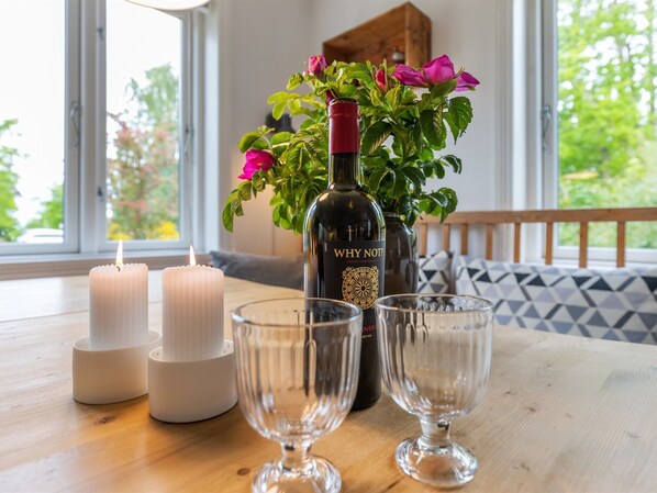 A table with candles, a bottle of wine, and glasses, with a window and a plant in the background.