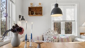 A dining area with a wooden table, candles, a vase with flowers, a wall-mounted shelf with decorative items, and a window with blinds. - "Anemette" - 100m from the sea by Interhome (Nexø)
