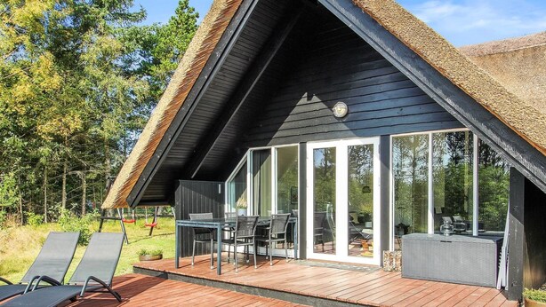 Una villa moderna con terrazza in legno, zona pranzo e ampia porta vetrata che dà su un giardino.