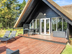 Eine moderne Villa mit Holzterrasse, Essbereich und einem großen Glasbau, der zum Garten führt.