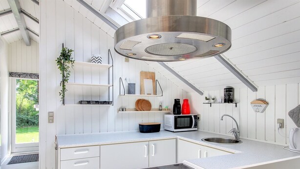 A modern kitchen with white cabinetry, a stainless steel range hood, a microwave, and a sink. - "Arnsten" by Interhome (Ansager)