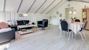A spacious loft with a high ceiling, a cozy seating area with a sofa and chairs, a dining table with chairs, and a decorative vase on the table. - "Arnsten" by Interhome (Ansager)