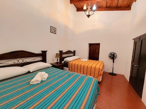 Une chambre avec deux lits, un ventilateur de plafond, une porte en bois et un lustre.