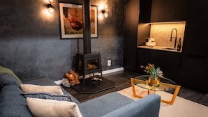A modern living room with a sofa, a glass coffee table, a fireplace, and a kitchen area with a sink and countertop. - Sambar Hills  (Cheshunt)