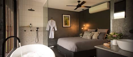 Ein modernes Schlafzimmer mit einem großen Bett, einer Badewanne, einem Deckenventilator und einem Badezimmer mit Dusche.