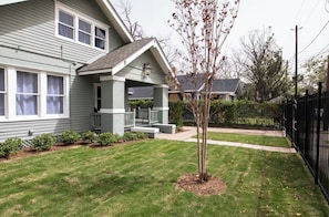 A residential house with a front porch, a small tree, and a well-maintained lawn.