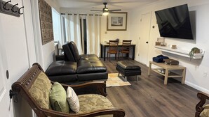 A living room with a sofa, ottoman, and chairs, a dining area with a table and chairs, and a TV mounted on the wall.
