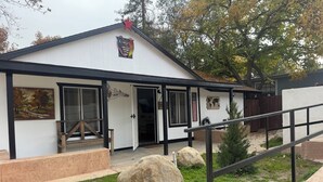 A building with a white exterior, black trim, and a star on the roof. There is a large rock in the front yard, and a wooden staircase leading up to the entrance.