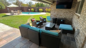An outdoor patio with wicker furniture, a pool, and a TV mounted on the wall.