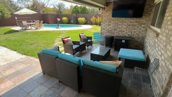 An outdoor patio with wicker furniture, a pool, and a TV mounted on the wall. - Spacious 4BR/3B, Fast WiFi, Gym, Ideal for Work, Near Dallas, Plano& Frisco (Carrollton)