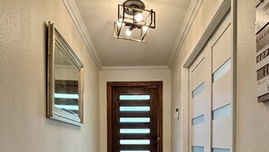 A hallway with a wooden door, a mirror, and a light fixture.