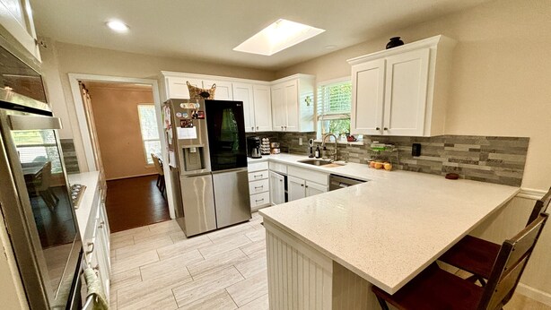 A modern kitchen with white cabinetry, a stainless steel refrigerator, a built-in oven, and a large island with bar stools.