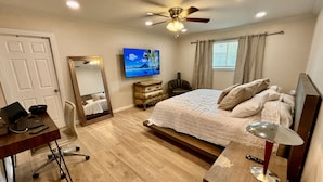A bedroom with a bed, a desk with a computer, a chair, a mirror, a ceiling fan, and a window with curtains.