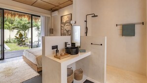 A modern bathroom with a large mirror, black sink, and shower. There is a bed with a view of a garden outside. - Exciting Chic 4BR Stylish Villa Next to Seminyak (Badung)