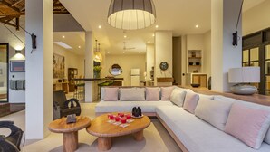A modern living room with a large sectional sofa, two wooden coffee tables, and a hanging pendant light. - Exciting Chic 4BR Stylish Villa Next to Seminyak (Badung)