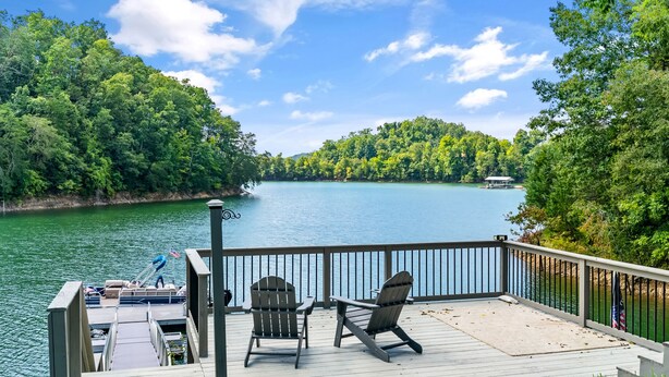 A deck with two Adirondack chairs overlooking a lake, surrounded by dense forest.