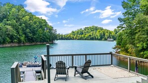 A deck with two Adirondack chairs overlooking a lake, surrounded by dense forest. - Relax with family and friends at this beautiful house on Douglas Lake.  (Dandridge)