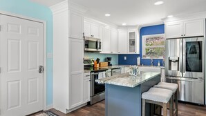 A modern kitchen with white cabinetry, a central island, stainless steel appliances, and a blue accent wall.