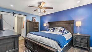 Een slaapkamer met een bed, nachtkastjes, een dressoir, een plafondventilator en een deur.