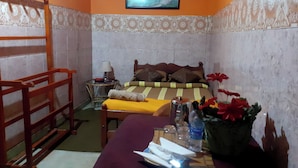 A small, cozy room with a bed, a wooden chair, a table with a lamp, and a painting on the wall. - Cool Land Hot Hut (Nuwara Eliya)
