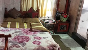 A bedroom with a bed, pillows, a nightstand, a lamp, and a small table with flowers. - Cool Land Hot Hut (Nuwara Eliya)