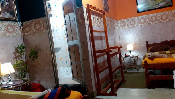A room with a bed, a chair, a table with a lamp, a ladder, and a door leading to a balcony. - Cool Land Hot Hut (Nuwara Eliya)