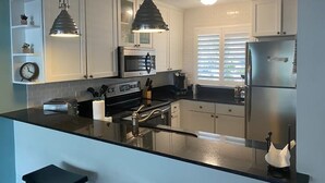 Una cocina moderna con armarios blancos, electrodomésticos de acero inoxidable, encimera negra e iluminación colgante.
