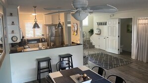 Una cocina moderna con una isla central, un comedor con mesa y sillas, y una escalera que conduce a un segundo piso.