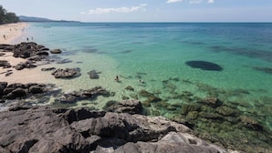 Een rotsachtige kustlijn met helder turquoise water en een zandstrand.
