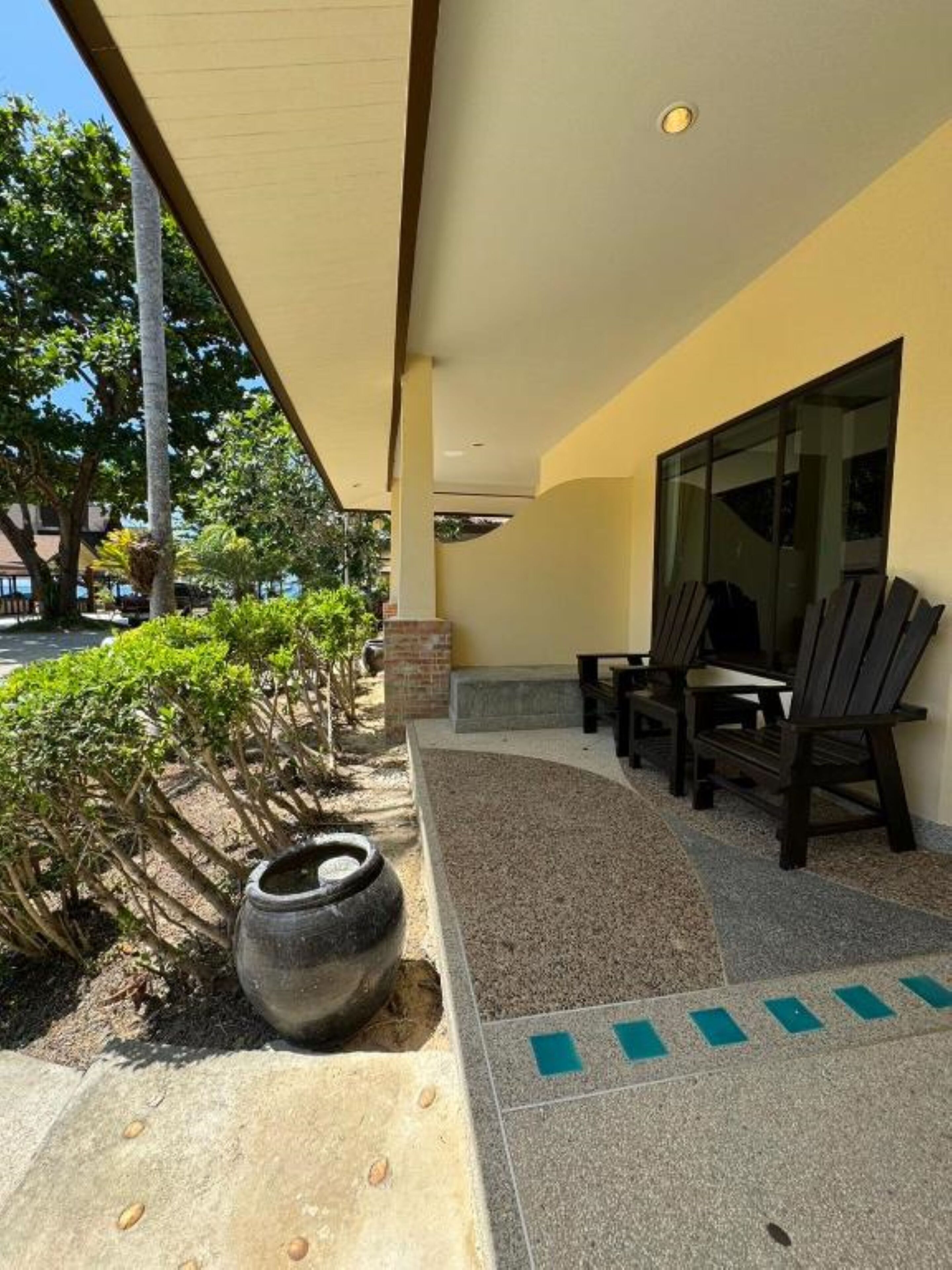 An outdoor seating area with a table and chairs, a large planter, and a pathway leading to a building entrance.