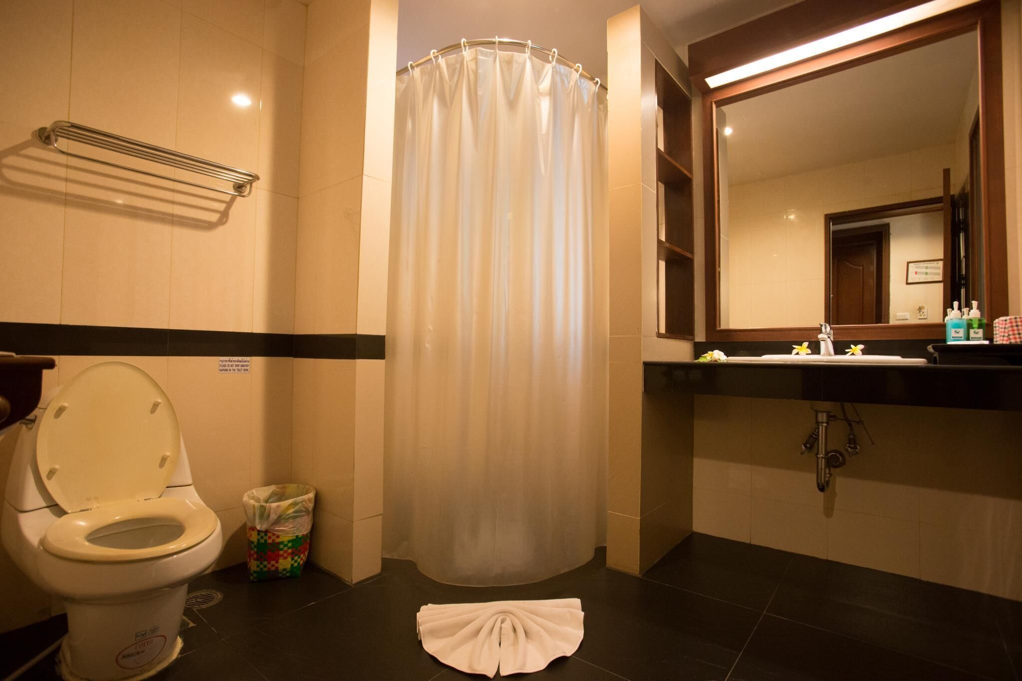 A bathroom with a toilet, shower curtain, sink, and mirror.